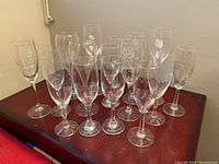 Front view showing 13 clear glass champagne flutes with floral etchings arranged on wood surface.