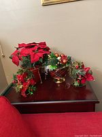 Front view of four vintage Christmas decorations on dark wood surface, showing red poinsettias, berries, and greenery accents.