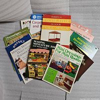 Photo showing 12 dollhouse miniature books and magazines with visible titles and colorful covers featuring dolls, miniature food, decorations, and plants.