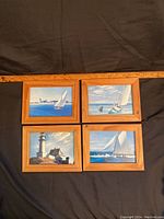 Overview of all four vintage nautical framed pictures lying on dark fabric with a ruler used for scale.
