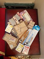Wide shot showing multiple vintage scrapbooking and junk journal supplies on a wooden surface including paper pads, wood stylus tools, ink pads, and small journals.