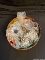 Photo of loose costume jewelry pieces inside a round container with plastic bags, including bracelets and necklaces.