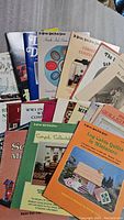 Photo showing a fanned out view of colorful vintage miniature dollhouse magazines with titles such as Christmas Confection, WWII Military Museum, and Canned Collectables.