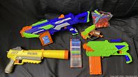 Three Nerf blasters with magazines, darts, and foam balls arranged on a black backdrop.