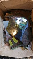 Box containing assorted painted scrap colored glass pieces with irregular shapes and various colors including yellow, green, red, blue, and brown.