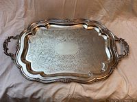 Top side of vintage silver plated serving tray showing detailed engraved floral pattern and ornate handles.