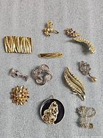 Full view of all ten vintage brooches and pendants with a mix of gold-tone and silver-tone finishes, showing designs ranging from floral to animal motifs with rhinestone and faux pearl accents.