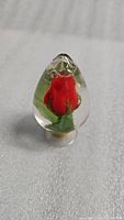 Front view of the clear resin piece showing a red rose bud encased inside, standing upright.