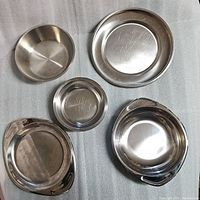 Top-down view of all 5 stainless steel bowls and plates showing different sizes and nesting capability, visible surface wear and scratches