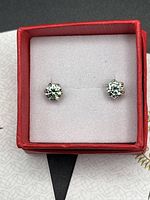 Pair of light blue Moissanite stud earrings set in sterling silver inside a red jewelry box with white cushion.