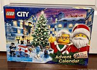 Front view of the Lego City Advent Calendar box showing festive winter city scene, Santa, woman in glasses, and Christmas tree. Displays age 5+, 258 pcs, and 24 gifts.