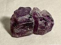 Two rough amethyst gemstones together showing their size and natural texture from one angle.