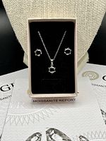 Jewelry set displayed in black velvet tray with GRA moissanite report certificates beneath, showing necklace and earrings with black moissanite stones in silver settings.