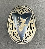 Front view of oval sterling silver brooch with central gold-tone Thai figure and filigree cut-out design