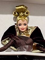 Close-up of Barbie doll face and upper body showing couture hairstyle and detailed costume.