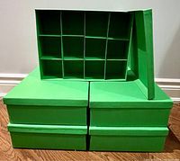 Five emerald green ornament storage boxes stacked in two rows; one box open showing 12 compartment grid inside.