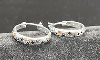 Front view of both silver hoop earrings showing sun, moon, and star zircon designs