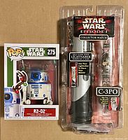 Front view of R2D2 Funko Pop #275 in box with Christmas antlers and Star Wars Episode 1 C3P0 lightsaber display case watch in clear plastic packaging.
