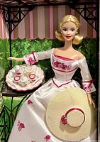 Barbie doll dressed in a white Victorian-style dress with red embroidery holding a hat and a detailed tea set on a tray.