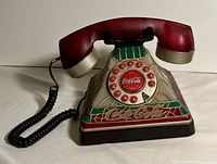Front view of Coca Cola stained glass style rotary dial telephone showing red rotary dial with Coca Cola logo, handset, and stained glass styled base.