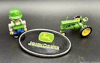 Group photo showing the belt buckle, miniature tractor missing a wheel, and Little People figure, all John Deere themed.
