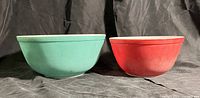 Photo of two vintage Pyrex mixing bowls, green and red exterior, positioned side by side on a fabric surface, showing their round shapes and color.