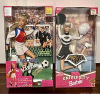 Both Barbie dolls shown in original unopened packaging. The 1998 Women's FIFA Soccer Barbie is on the left wearing soccer attire and holding a soccer ball; the 1996 Purdue University Cheerleader Barbie is on the right wearing a cheerleading uniform and holding pom-poms.
