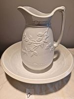 Photo of the white antique ceramic jug and matching basin with visible embossed floral design showing overall condition and appearance.