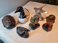All six figurines displayed together on a surface: wooden duck, large resin loon, pewter goose on swivel rock, two ceramic owls, small resin loon