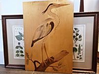 Wooden heron parquet artwork with two framed botanical prints behind it