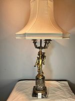 Full view of the brass and marble lamp with cherub figure and fabric shade on top.
