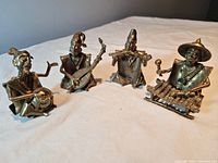 Four handcrafted brass musicians figurines arranged in a row, each holding a traditional musical instrument.