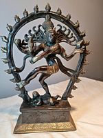 Front view of brass Shiva statue with dancing Nataraja pose inside circular flame halo, standing on detailed base.