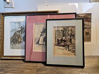 Four framed prints and drawings grouped together resting against a wall, showing size variation and framing style.