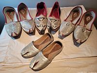 All four pairs of handmade East Indian leather shoes laid on a white cloth, showing metallic silver thread embroidery with traditional patterns, including red trim on many pairs.