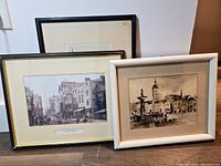 Three framed prints grouped together showing city scenes, different frames and minor water damage on one print.