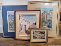 Four framed artworks grouped together with different sizes and frame styles, showing varied streetscape and architectural scenes.