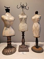 Photo showing three mannequin-style jewelry holders with various handcrafted materials: ceramic, resin, paper mache, wood bases, and metal hooks.