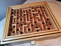 Top-down view of the wooden marble maze showing the intricate pathways, holes, metal marble, and control knobs