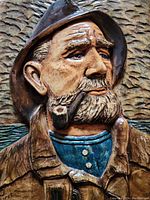 Close-up photo of the ceramic sea captain plaque showing detailed face, hat, coat, and pipe against textured background.