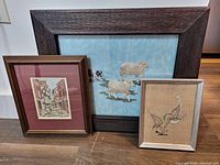 Three framed needlework artworks displayed together on a flat surface.