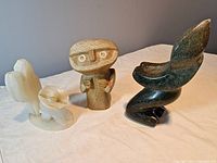 Photo showing all three hand-carved stone figures together on white cloth: Shona soapstone figure on right, yellow stone figure center, onyx figure on left