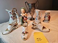 Group photo of ceramic and porcelain items including figurine, trophy, jugs, and bone china shoes on a table.
