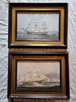 Two framed antique ship prints with wire hooks visible, showing front view of both framed prints stacked vertically.