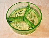 Photo of green uranium glass dish showing the round shape with three internal dividers and starburst pattern on the bottom, in normal lighting.