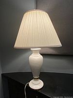 Single white marble table lamp with pleated cream shade, on black surface.