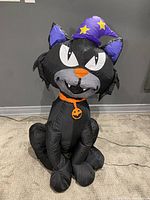 Front view of the black cat inflatable in working condition showing full details including face, hat, collar, and body posture.