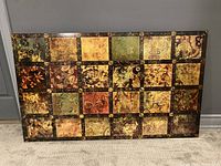 Front view of rectangular Bombay Company wall art showing 24 square segments with varied designs in warm earth tones and dark wood frame.