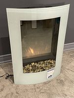 Front view of built-in wall electric fireplace showing curved frosted white glass front with pebble bed and flame effect.