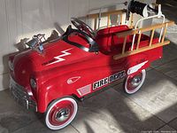 Three-quarter front view of red pedal car showing body graphics, wheels and bell